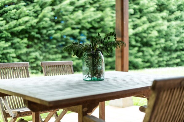 A wooden table with a glass vase containing green plants, surrounded by wooden chairs. - Villa San Antolo Villahormes (Llanes)