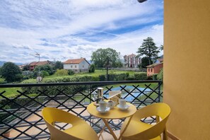 A balcony with yellow chairs and a small table, overlooking a garden and buildings. - El Rincon de las Americas (Colombres)