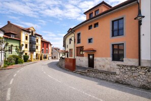 A quiet street lined with colorful buildings, a clear sky, and a stone wall along the sidewalk. - El Rincon de las Americas (Colombres)