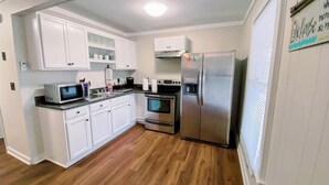 Una cocina con armarios blancos, un refrigerador de acero inoxidable, un microondas y un horno.