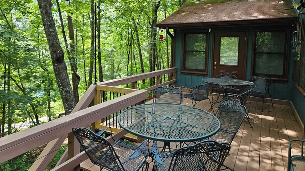 A wooden deck with a round metal table and chairs, surrounded by trees. - The Nest is Best in Bear Paw, Murphy, NC.  (Murphy)
