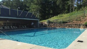 A rectangular swimming pool with clear blue water, surrounded by a concrete deck. There are lounge chairs and a building with a sloped roof in the background. - The Nest is Best in Bear Paw, Murphy, NC.  (Murphy)