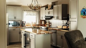Una cocina con armarios blancos, encimera de madera, horno empotrado y una lámpara de araña.