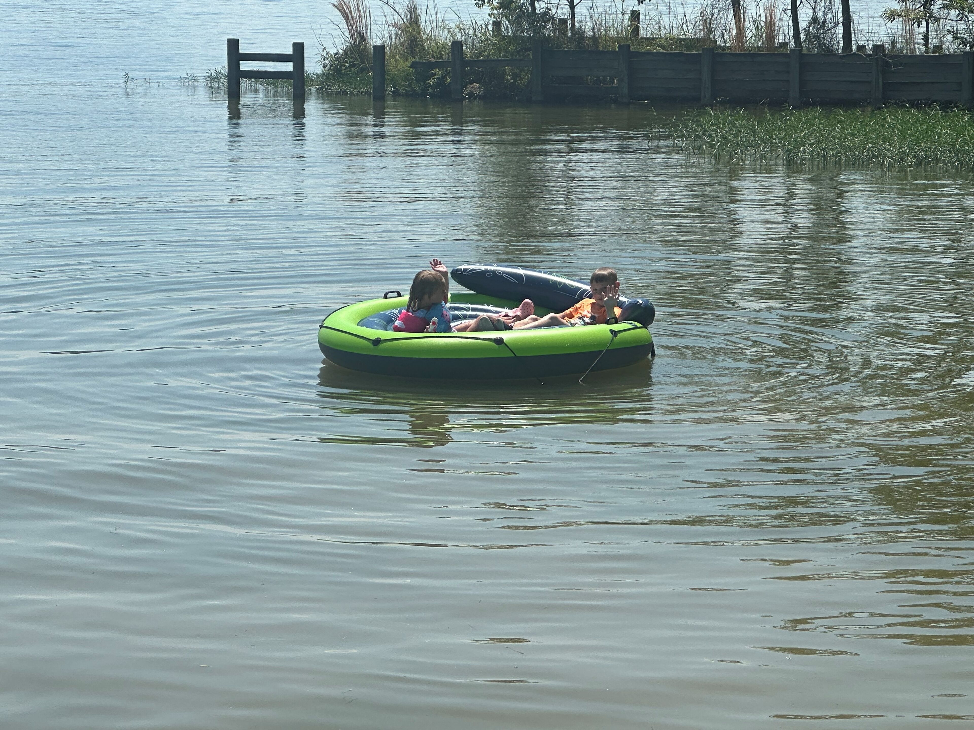 A green inflatable raft with people on it floating on calm water.