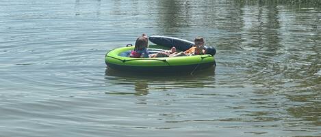 A green inflatable raft with people on it floating on calm water.