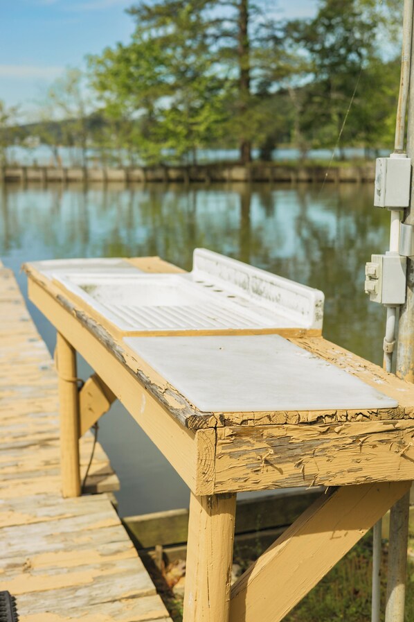 A wooden bench with a white surface, positioned on a wooden dock extending over a body of water, with trees in the background. - Cozy hideaway on Weiss Lake
with private dock and kayaks! (Cedar Bluff)