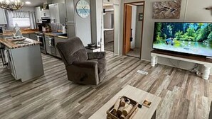 Una sala moderna con un sofá gris, un televisor y piso de madera.