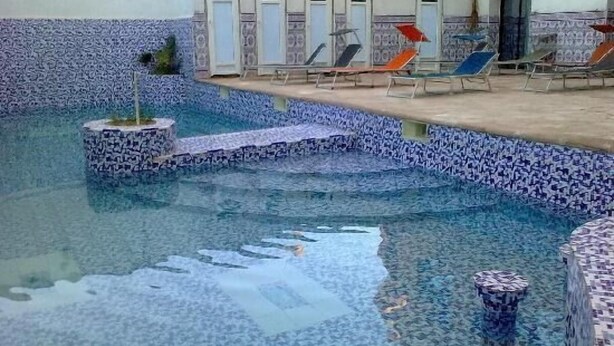 Une piscine dont le bord est revêtu de carreaux, avec des chaises longues et des portes le long du côté.