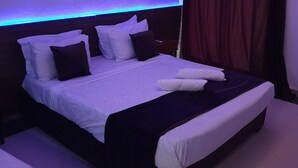 A neatly made bed with white and dark pillows, a dark headboard, and a blue ambient light strip. - Le Privilege (Bir El Djir)