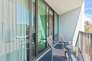 A balcony with a table and chairs, a sliding glass door, and a view of the street.