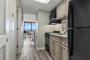 A kitchen with a black refrigerator, a microwave, and a stove. There is a dining area with a table and chairs visible through an open door. - Pinnacle 755 Oceanfront Tower (Myrtle Beach)