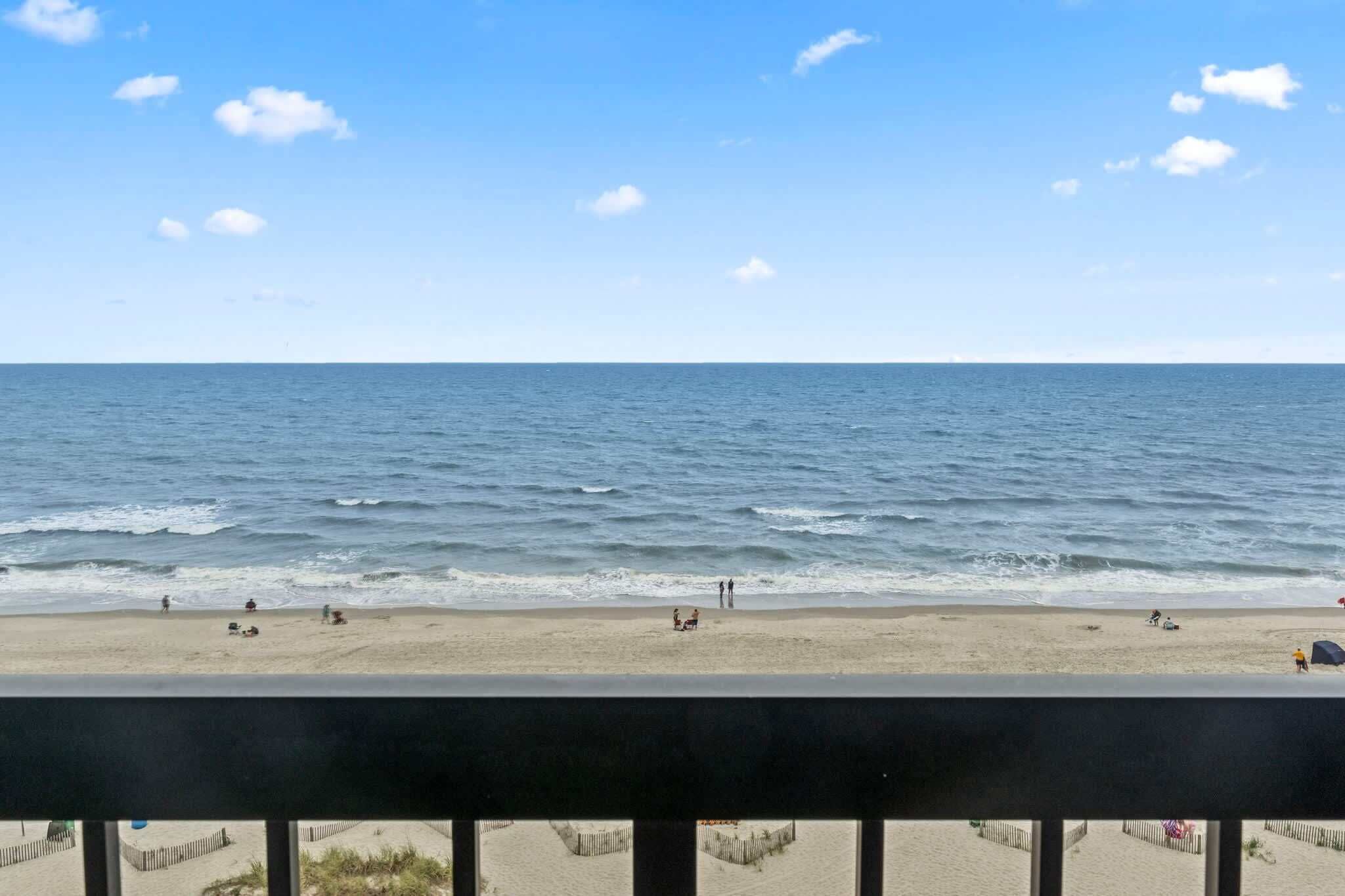 A beach view with a clear sky, calm sea, and a few people on the sand.