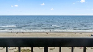 Een uitzicht op het strand met een heldere lucht, rustige zee en enkele mensen in het zand.