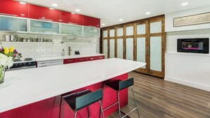 A modern kitchen with a white island, red cabinets, and a wooden floor. - Riverfront Studio - Private Patio & Pet Friendly! (Bend)