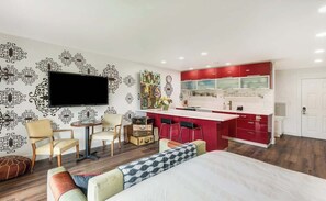 A compact room with a bed, a TV, a small dining area, and a kitchenette.