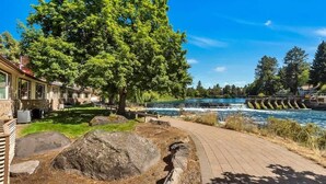 A riverside walkway with a wooden deck, large rocks, and a tree. - Riverfront Studio - Private Patio & Pet Friendly! (Bend)