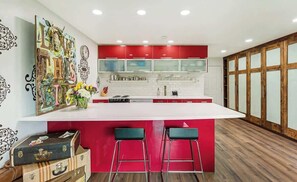 A modern kitchen with a large island, red cabinetry, and two bar stools.