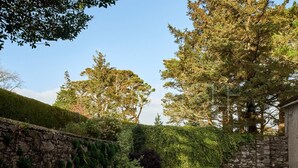 Eine Steinsäule mit einer Bank, einer gepflasterten Terrasse und einer Hecke.