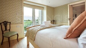 Ein Schlafzimmer mit einem großen Bett, einem Sessel, einem Fenster und einer Tür zu einem anderen Raum.