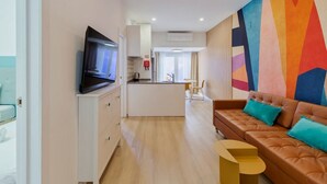 Ein modernes Wohnzimmer mit einem braunen Ledersofa, einem an einer Kommode befestigten Flachbildfernseher, einem kleinen gelben Beistelltisch und farbenfroher abstrakter Wandkunst.