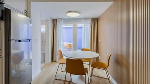 Eine moderne Küche mit einem Einbaukühlschrank, einem runden Esstisch mit vier Stühlen und Blick ins Freie durch große Fenster.