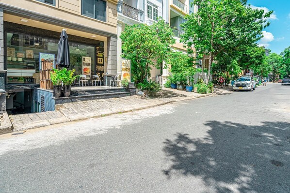 A street with a restaurant on the left, outdoor seating, and parked cars.