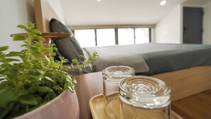Une chambre moderne avec un lit, une petite table sur laquelle est posée une plante en pot, et deux verres transparents sur un plateau.
