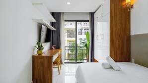 Une chambre d’hôtel comprenant un lit, un bureau, une chaise, une télévision et un balcon avec vue sur les bâtiments.