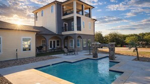 A two-story house with a pool, outdoor seating, and a stone bridge.
