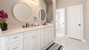 A bathroom with two sinks, white cabinets, a large mirror, and a potted plant.