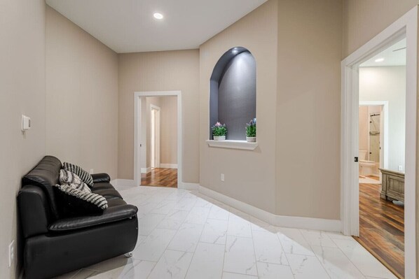 A spacious living room with a black leather sofa, a large window with a view, and a wooden floor.