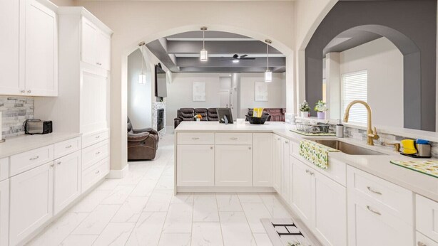 A modern kitchen with white cabinetry, a central island, and a dining area with leather chairs.