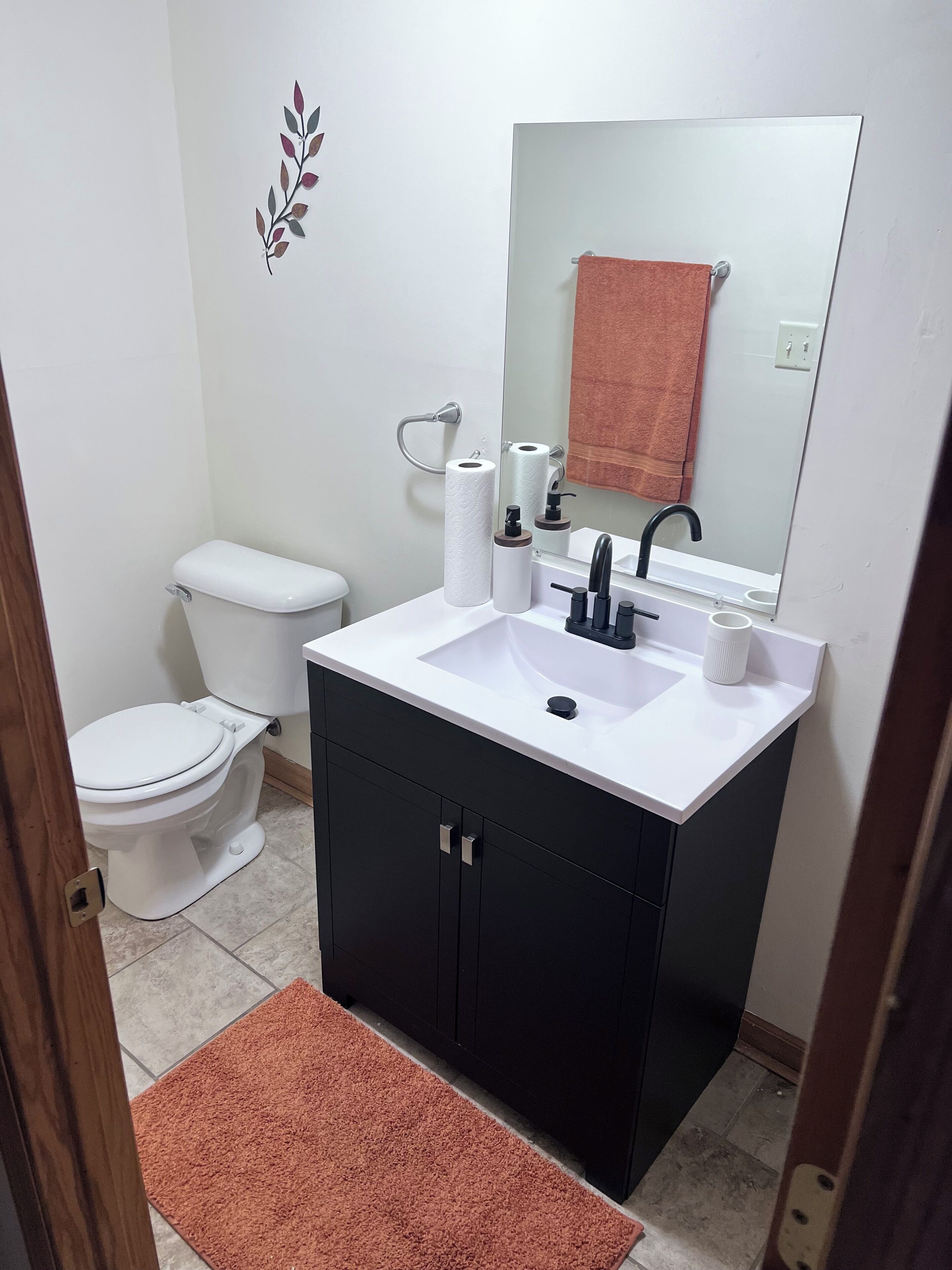 A bathroom with a white toilet, a sink with a mirror, and a brown rug.