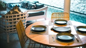 A round wooden table with four black plates and cutlery, surrounded by wicker chairs. - CALM VILLA SEMINYAK (Seminyak)