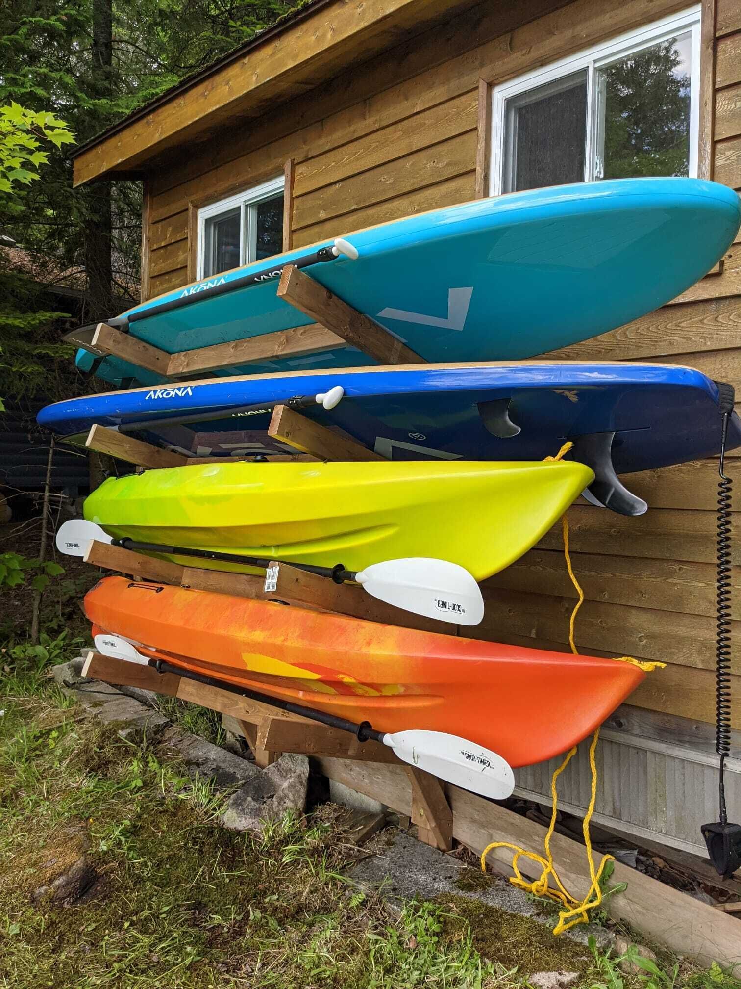 A row of kayaks leaning against a wooden cabin wall.