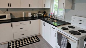 A kitchen with white cabinets, a black countertop, a microwave, a toaster, a sink, and a stove.