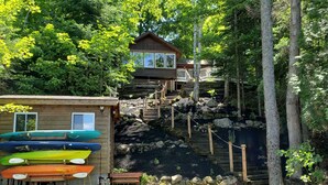 A cabin with a wooden deck and a small dock, surrounded by dense forest.