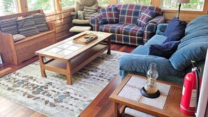 A cozy cabin interior with wooden walls, a plaid sofa, a wooden bench, and a fire extinguisher.