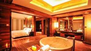 Una habitación de hotel moderna con piso de madera grande, una bañera de mármol, una cama, un baño con espejo amplio y un banco de madera con velas.