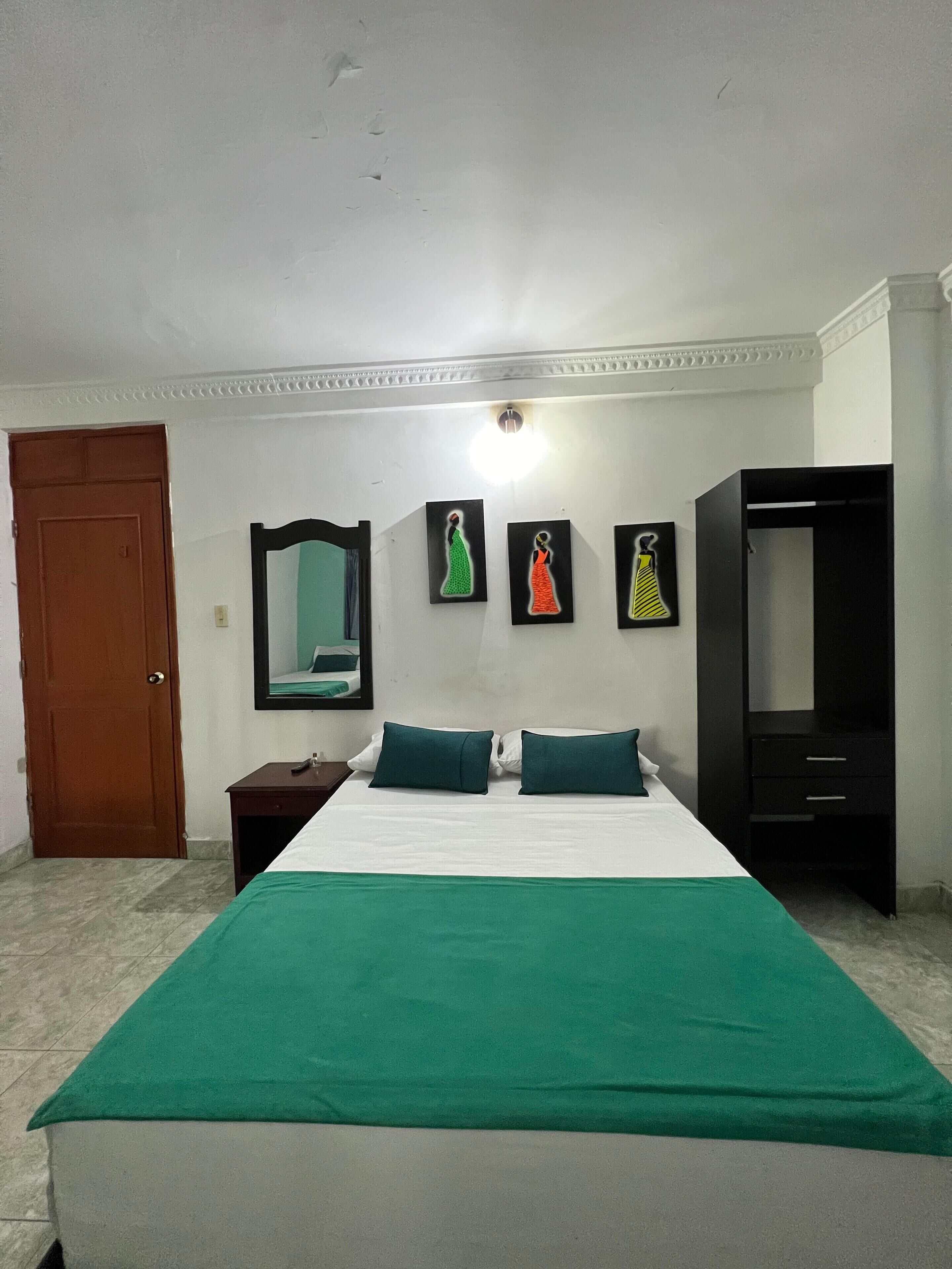 A hotel room with a bed, a wardrobe, a nightstand, and three wall-mounted paintings.