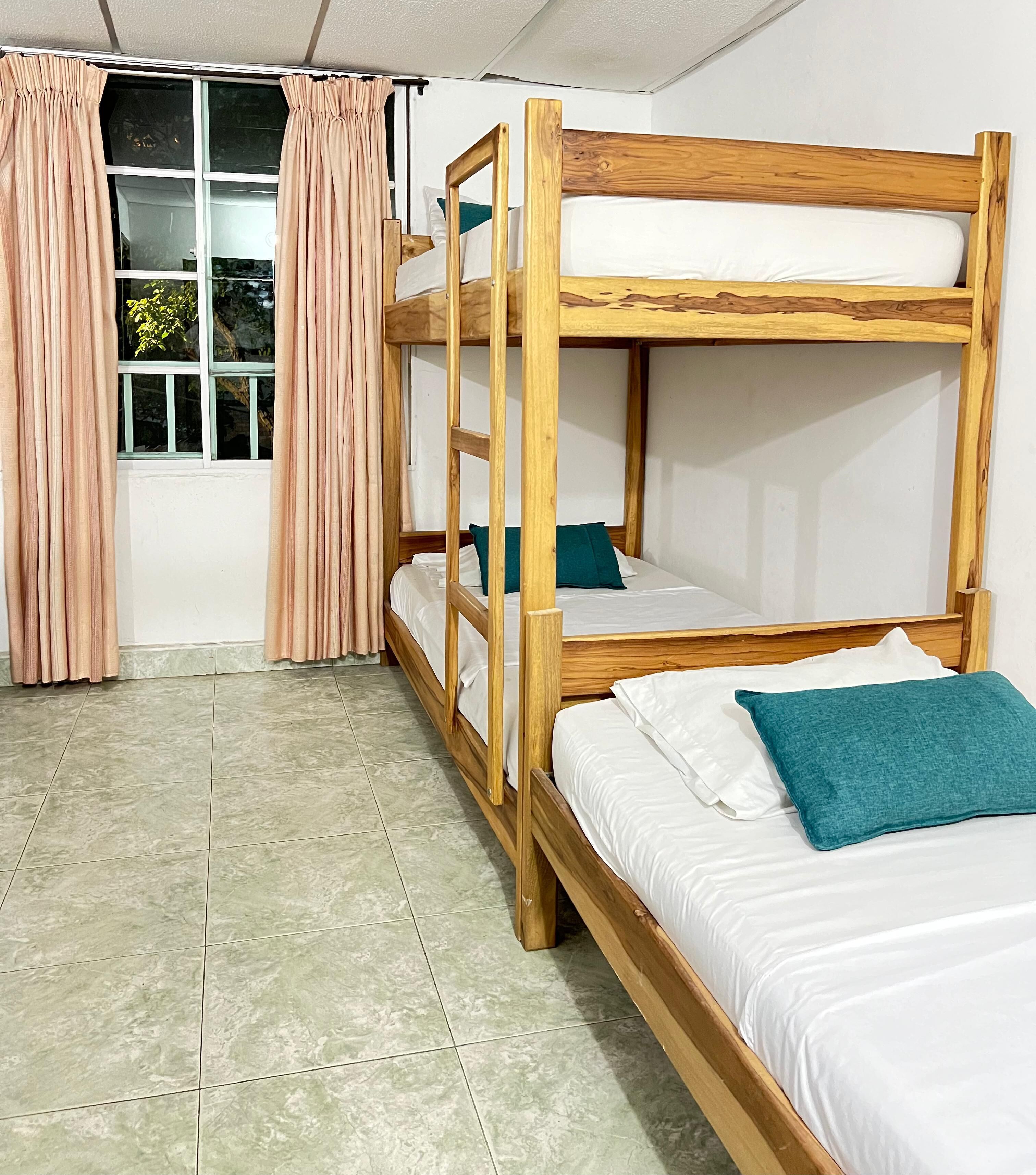 Dormitorio con literas, ventana, cortinas y suelo de baldosas.