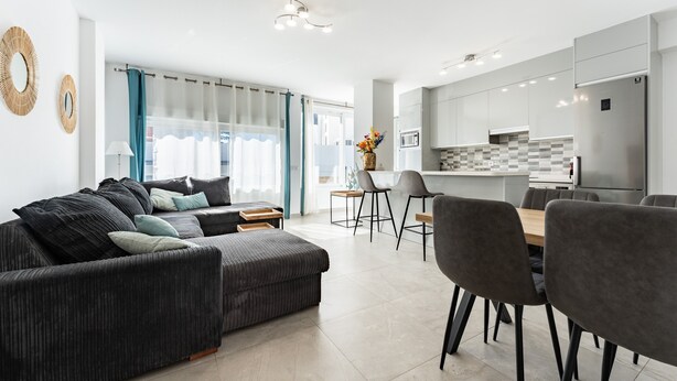 Una sala moderna con sofá, mesa de comedor, sillas y una cocina con armarios y electrodomésticos.