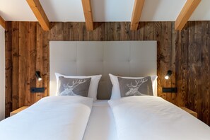 Un lit double avec une tête de lit en bois, deux lampes fixées au mur et deux oreillers ornés de motifs de cerfs.