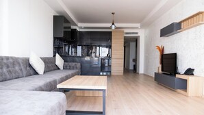 A modern living room with a grey sofa, a wooden coffee table, and a TV on a wooden stand. - Si Hotel & Spa (Kuşadası)