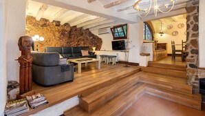 A living room with a stone wall, a fireplace, a staircase, and a chandelier. - Holiday Home 'Casa Rústica Cal Mian' with Mountain View, Wi-Fi and Air Conditioning (Almoster)