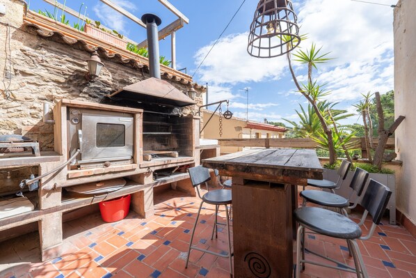 Una cocina al aire libre con una parrilla, una mesa de madera y sillas.
