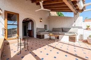 Un patio al aire libre con techo de madera, puerta de cristal, un sofá, una mesita y una planta en maceta.