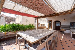 Un patio al aire libre con mesa y sillas de madera, piso de ladrillo y plantas en macetas.