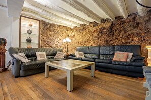 A cozy living room with a stone wall, two leather sofas, a coffee table, and a small shelf with decorative items.