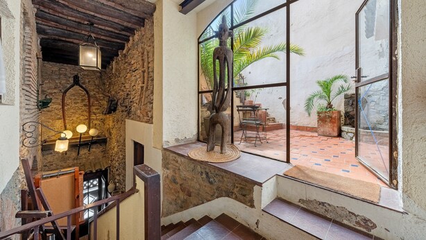 A staircase with a stone wall, a wooden railing, and a view of an outdoor patio with a statue and plants. - Holiday Home 'Casa Rústica Cal Mian' with Mountain View, Wi-Fi and Air Conditioning (Almoster)